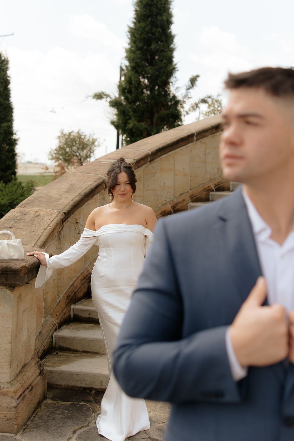 Wedding couple poses on stone steps with bride in elegant white dress and groom in navy suit.