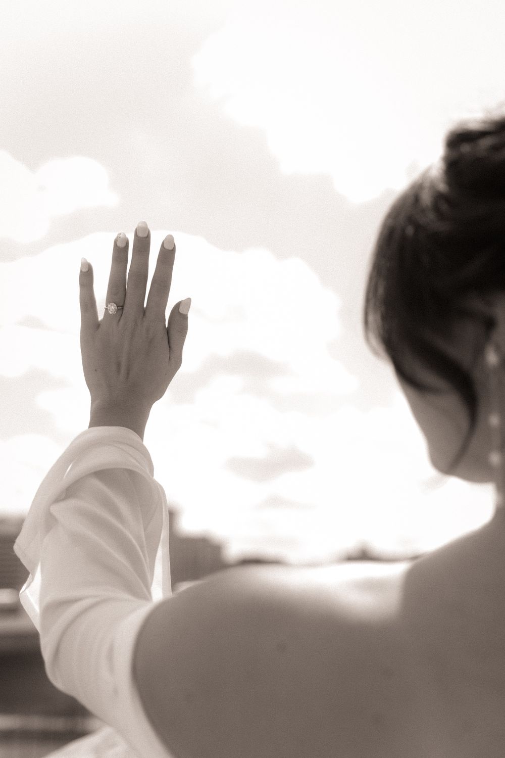 A sepia-toned image of someone raising their hand toward the sky with clouds in the background.