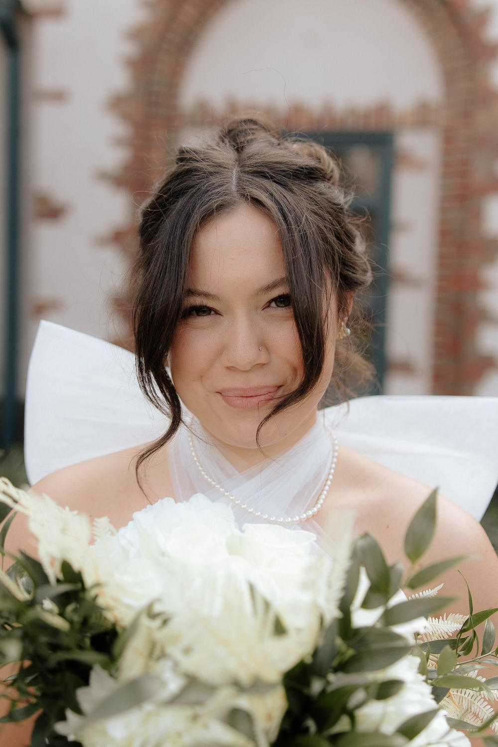 A beautiful wedding bouquet features white roses and delicate greenery against a brick archway.