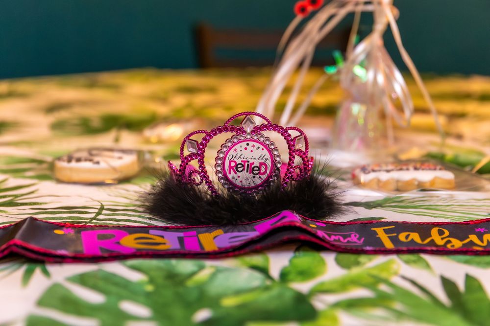 A sparkly pink tiara with black fur trim rests on a colorful party tablecloth with decorations in the background.