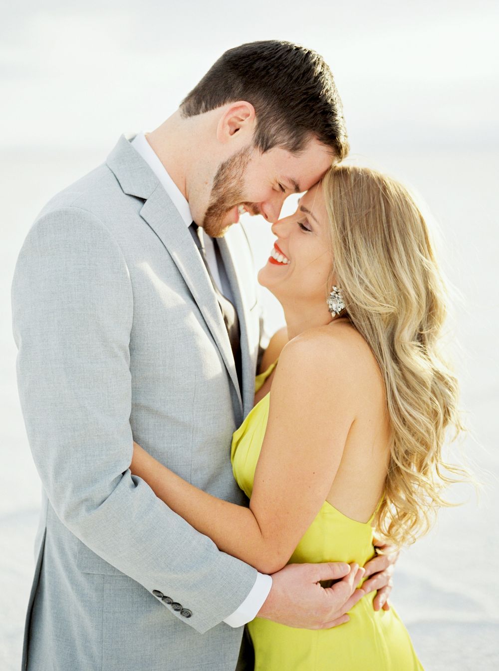 Romantic couple in formal attire sharing an intimate moment, with her in a yellow dress and him in a grey suit.