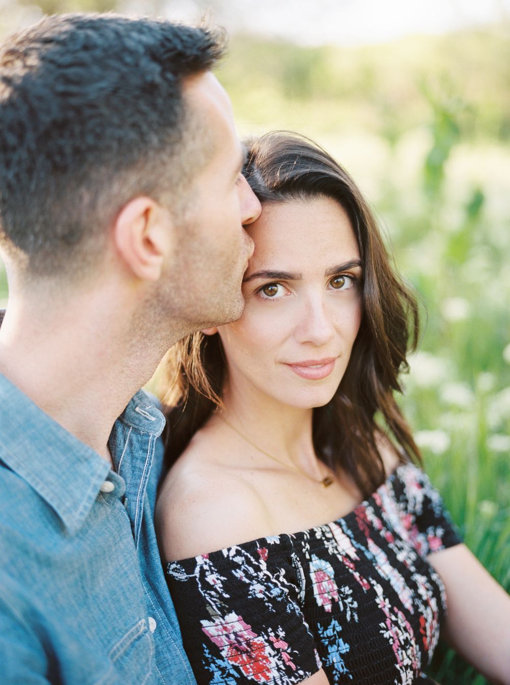 Romantic couple in casual attire posing among spring flowers and greenery.