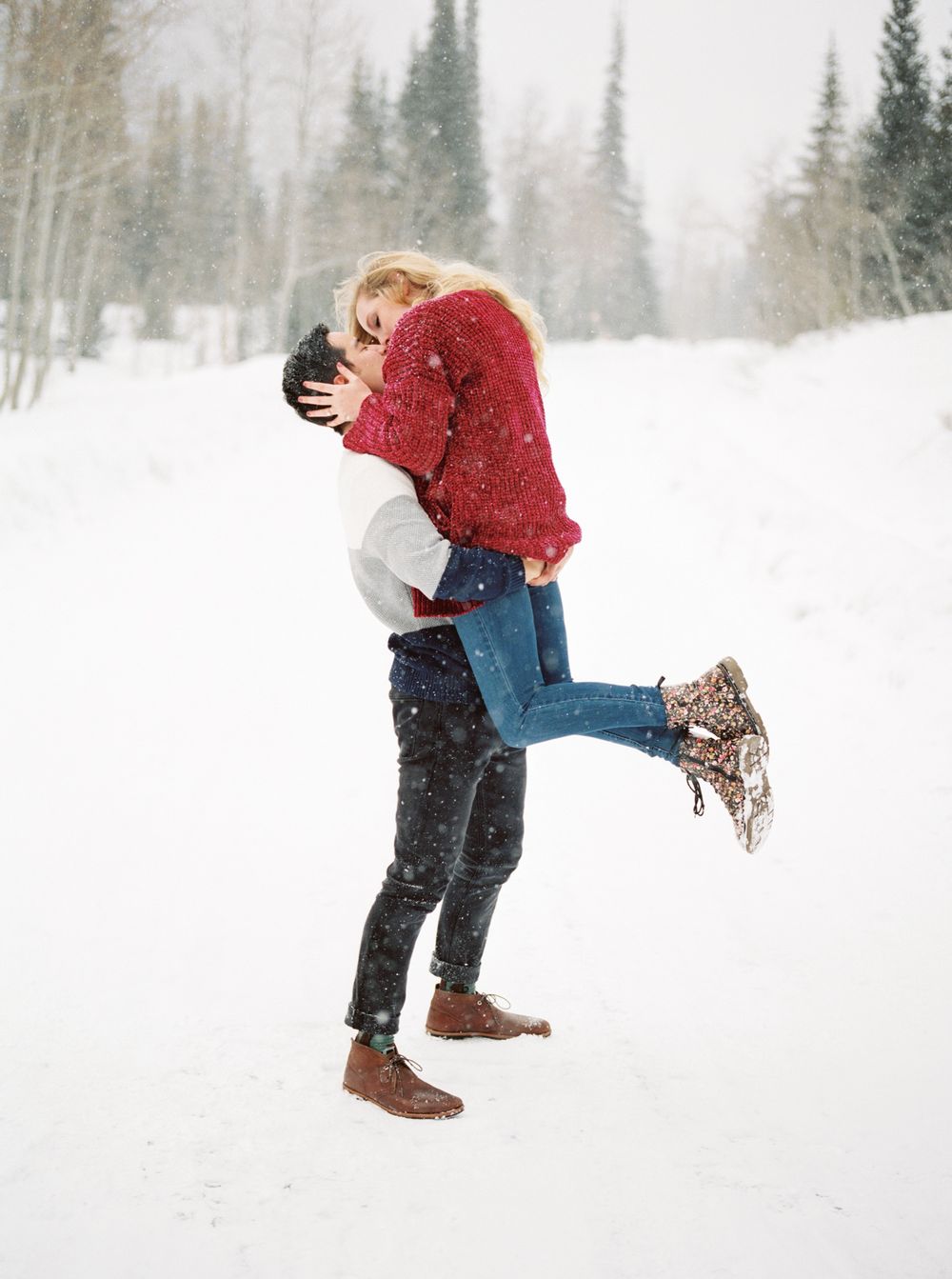 Couple sharing a romantic moment in the snowy wilderness with pine trees behind them.
