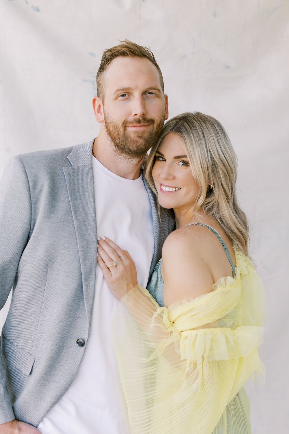 Couple poses together with woman wearing yellow off-shoulder dress and man in gray blazer.