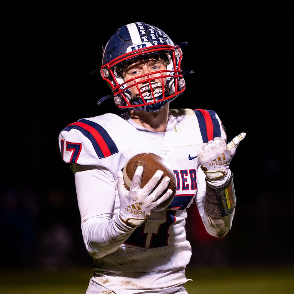 Football player in white and navy uniform catches ball during nighttime game.