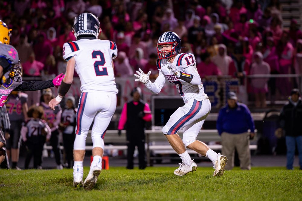 Two football players in white uniforms communicate during night game on illuminated field.