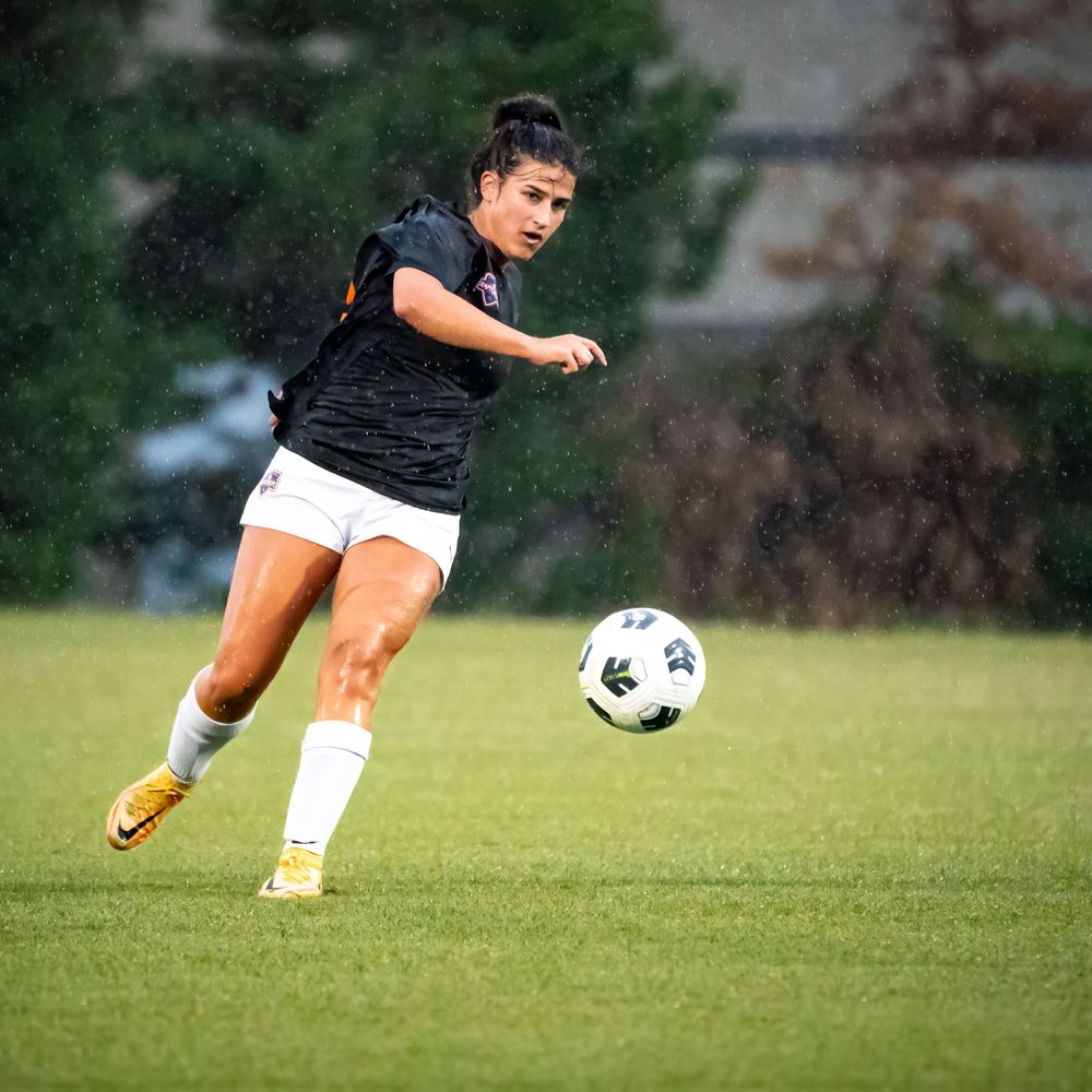 Soccer player in black jersey dribbles ball across green grass field during match.