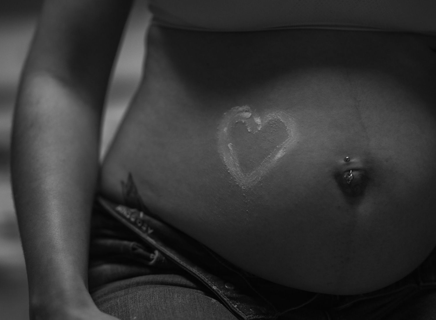 Black and white close-up of a bare pregnant belly with a heart drawn on the skin.