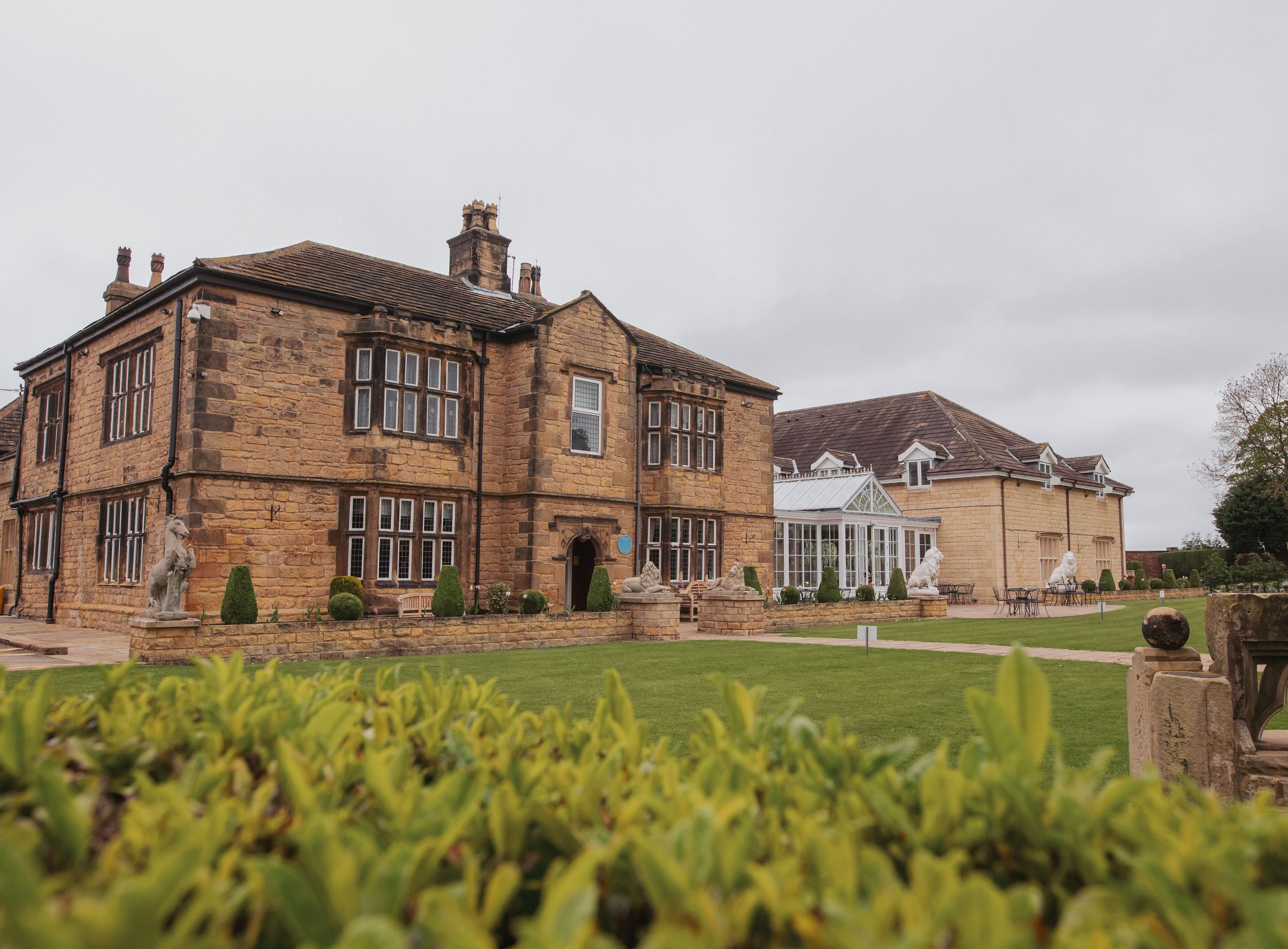 Elegant stone manor house with ornate architecture and manicured gardens viewed from ground level.