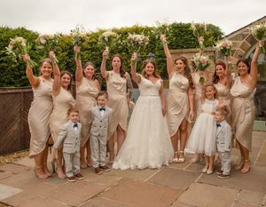 Wedding party poses together outdoors in champagne-colored dresses and formal attire.