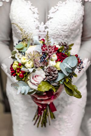 A winter-themed bridal bouquet featuring roses, pinecones, and eucalyptus with burgundy accents.