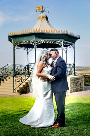 Romantic wedding photoshoot series under an ornate gazebo with decorative metalwork against a scenic landscape background.