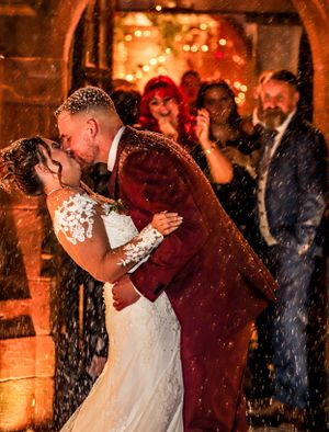A romantic wedding kiss moment captured in front of warm glowing lights with falling snow.