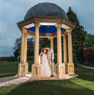 Romantic evening photo in a classical stone gazebo with domed roof in a garden setting.