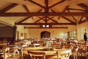 An empty rustic wedding reception venue with exposed wooden beams and round tables.