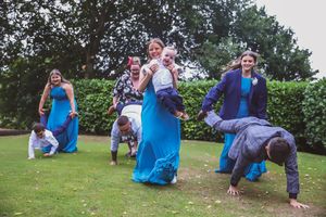 Wedding party members playing and posing on grassy lawn wearing bright blue outfits.