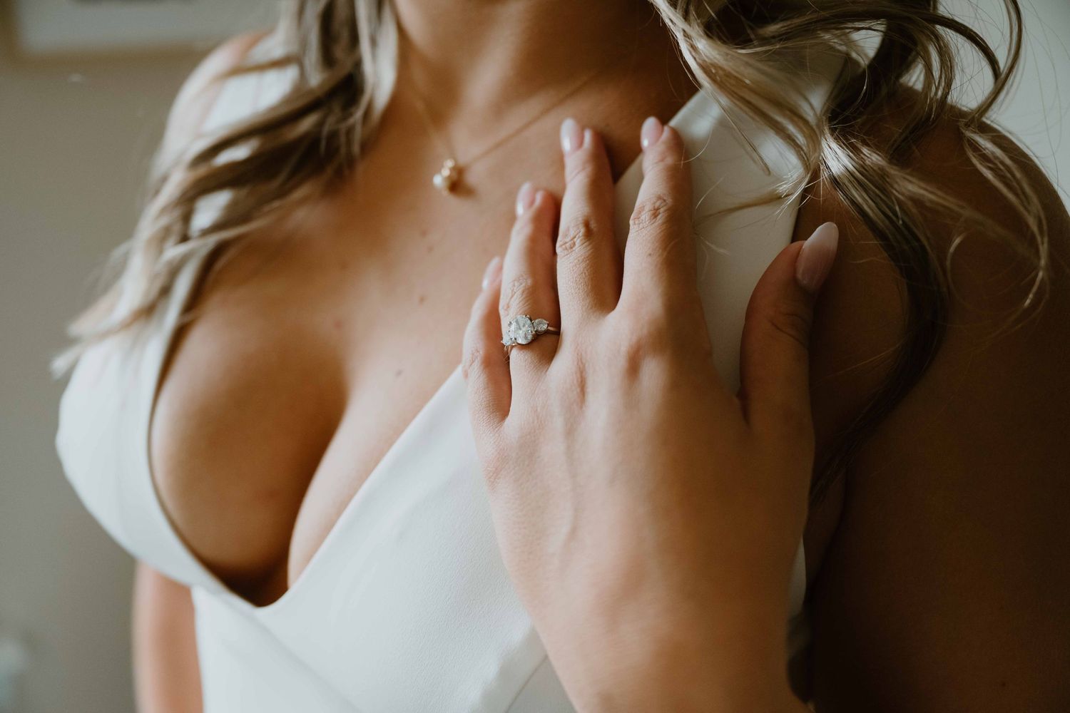 Close-up of bride in white gown showcasing stunning diamond engagement ring and delicate necklace.