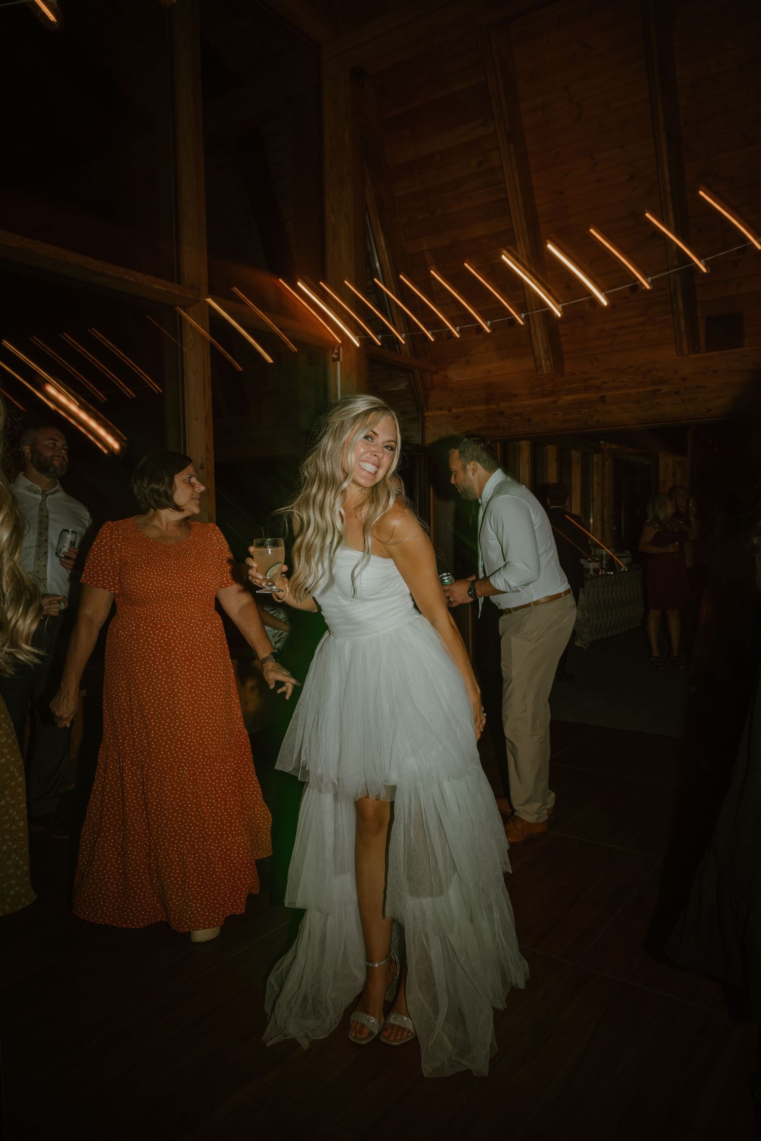 Smiling bride in white tulle dress enjoys dancing at rustic barn wedding reception.