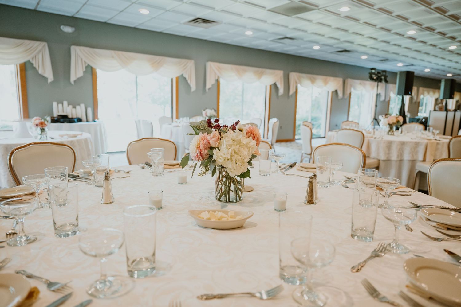 Elegant wedding reception venue with round tables, white linens, and floral centerpieces in soft pink tones.