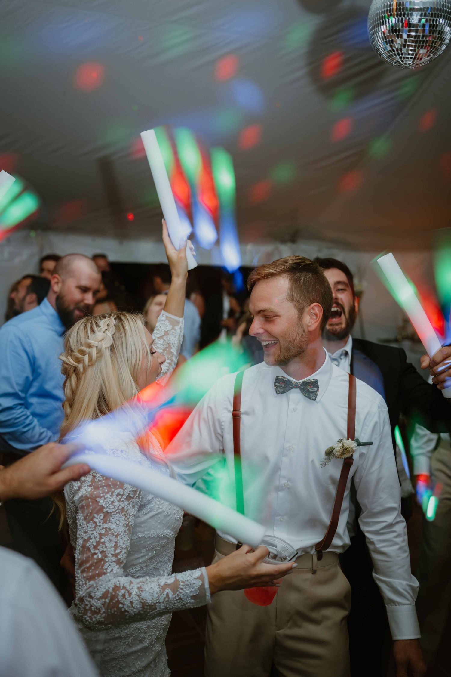 Bride and groom dancing with colorful LED glow sticks under a disco ball at their wedding reception.