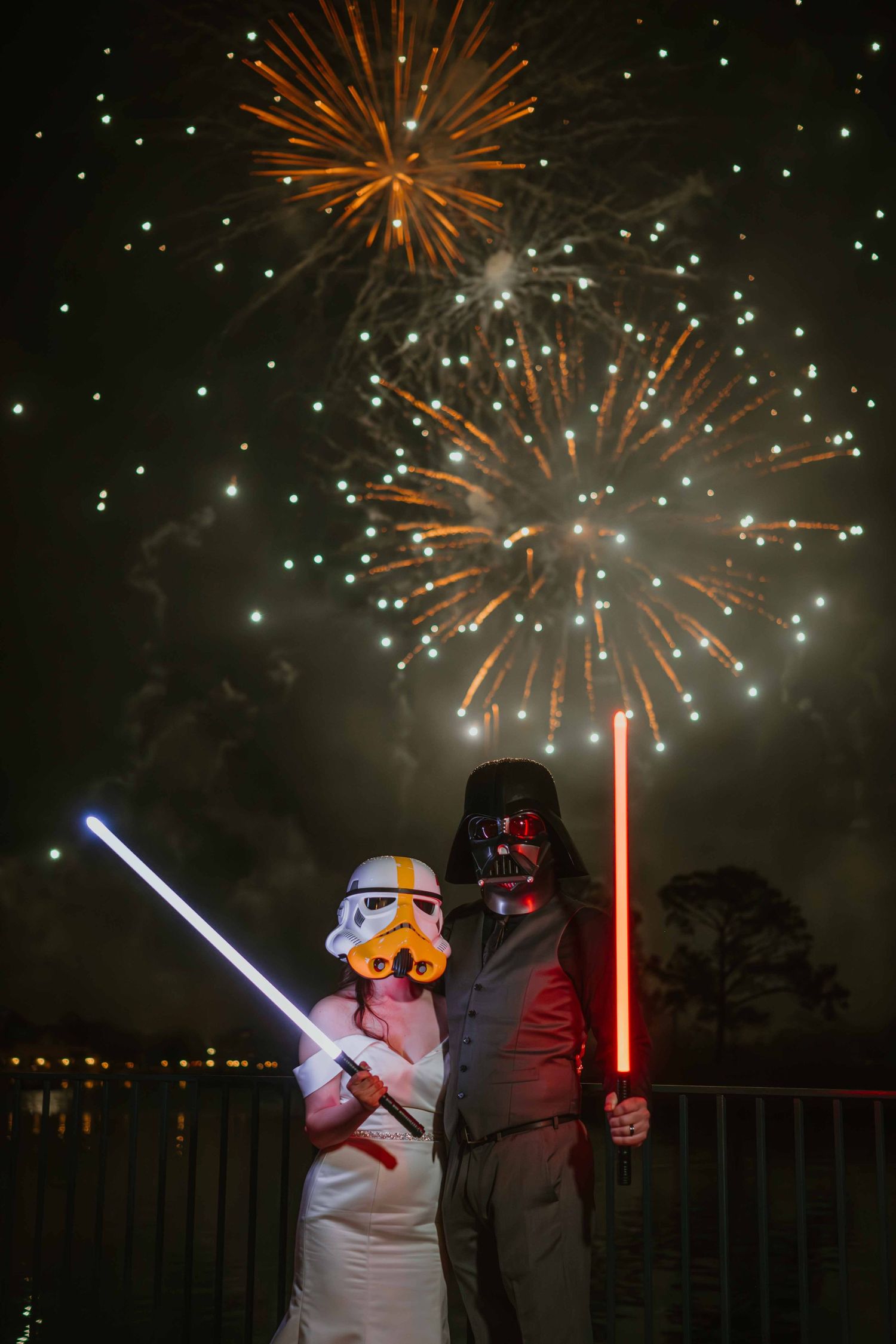 Star Wars themed wedding couple in Stormtrooper and Darth Vader masks holding lightsabers with fireworks display.