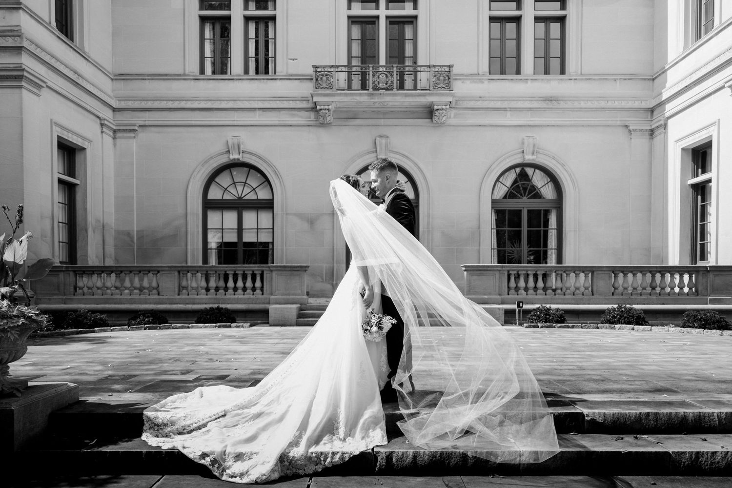 Dramatic black and white wedding photo of couple kissing with veil billowing in wind.