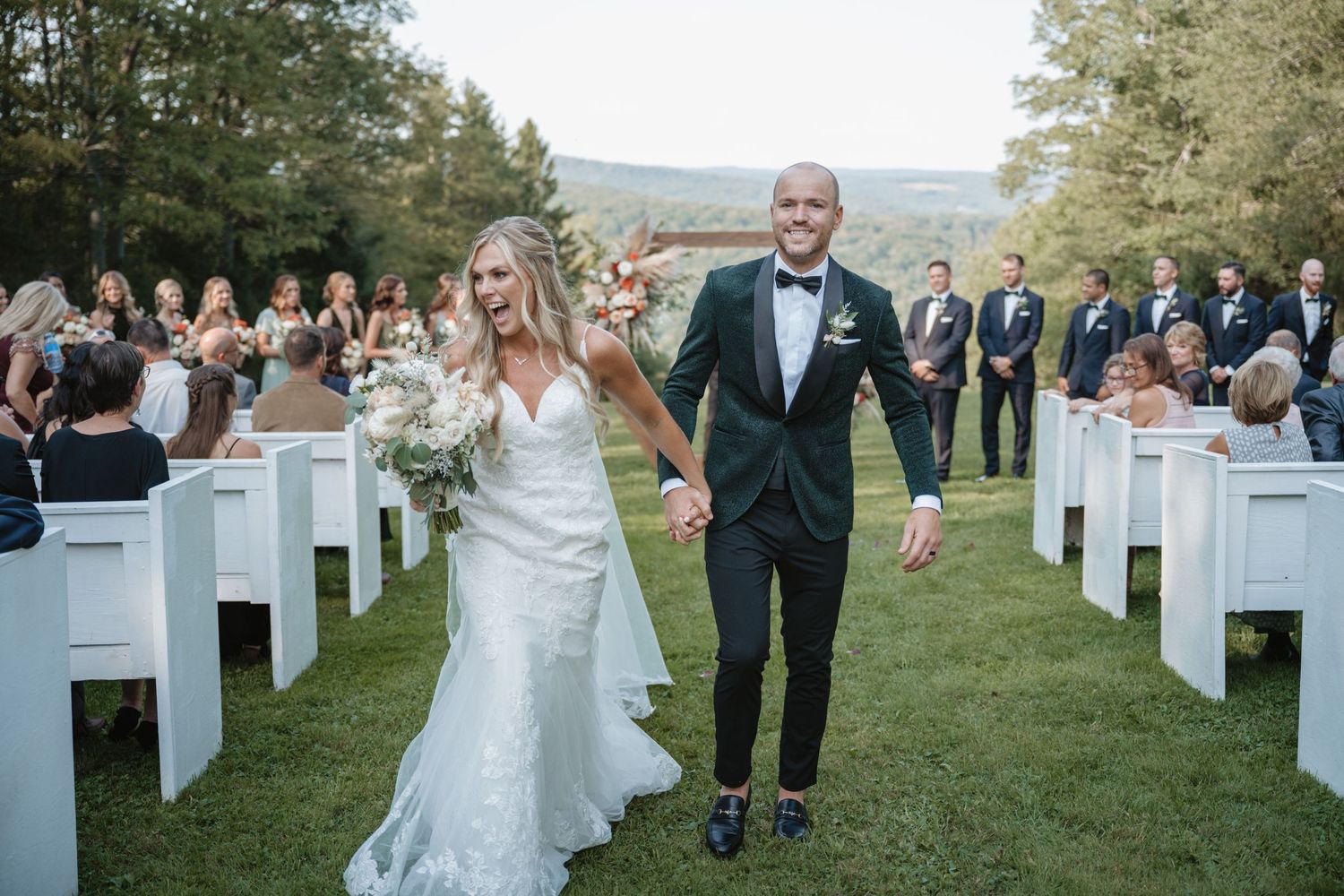 Bride and groom walking down outdoor aisle after wedding ceremony on a green lawn.