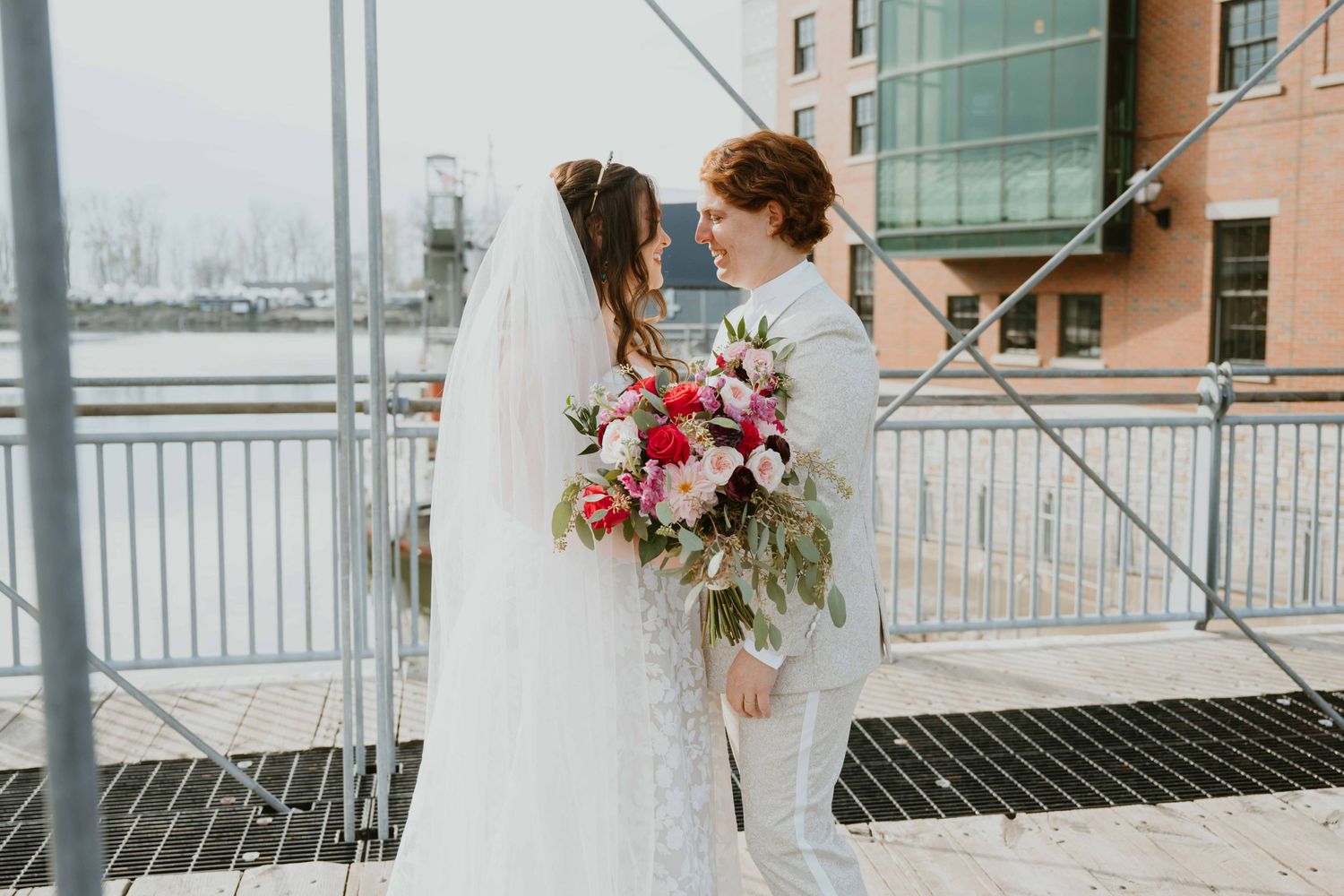 Bride and groom share intimate moment on bridge with colorful bouquet and veil.