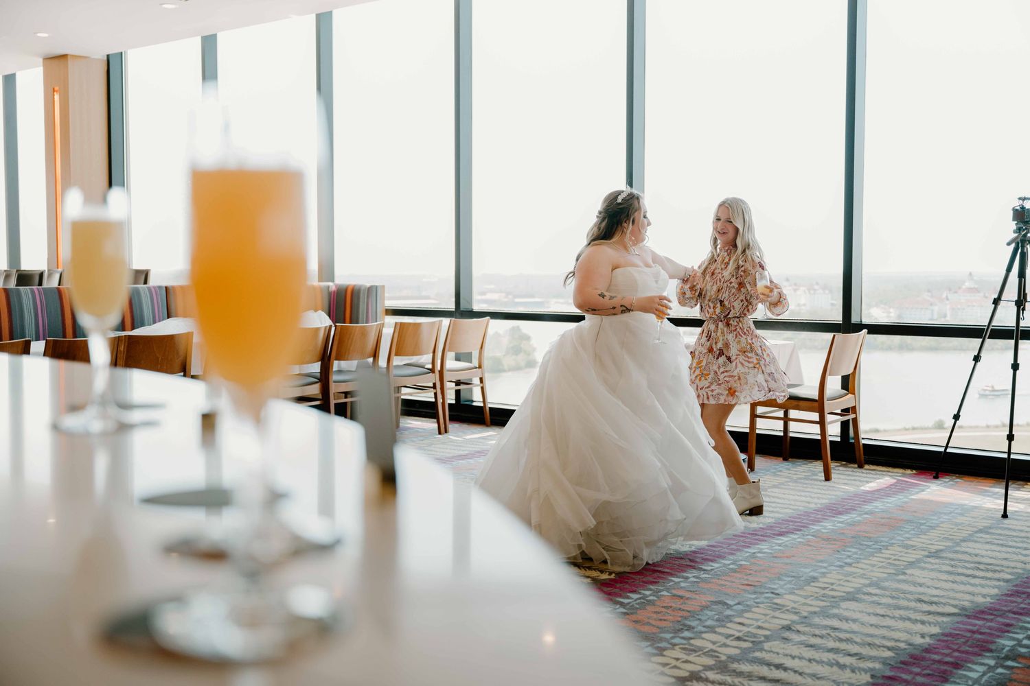 Bride in full white tulle gown dancing with guest near large windows at Disney resort reception.