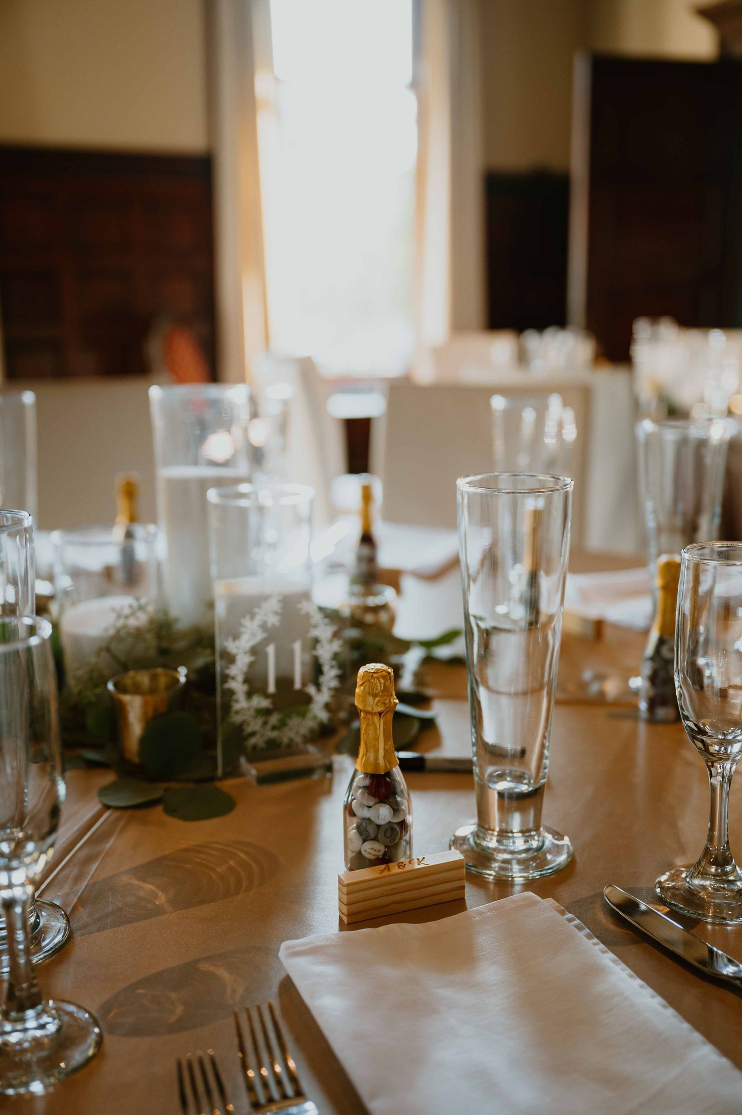 Elegant wedding reception table set with champagne bottles, candles, and glassware centerpieces.