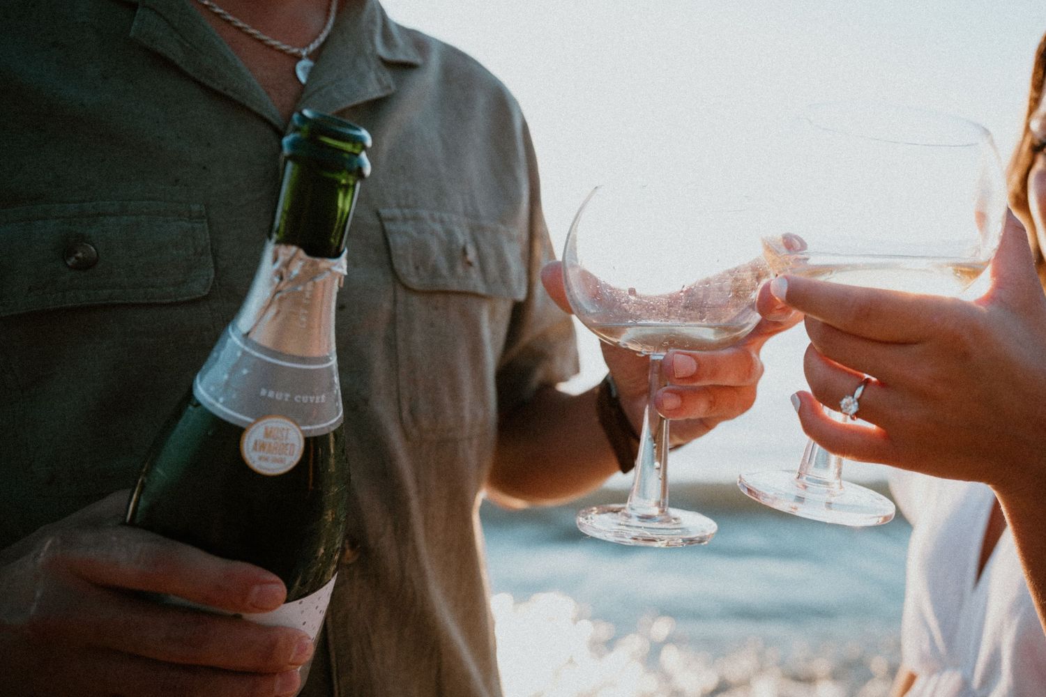 Couple pours champagne into glasses during a romantic beach engagement celebration at sunset.
