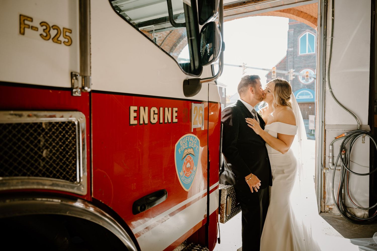Bride and groom share a kiss beside a red fire engine F-325 inside the firehouse.