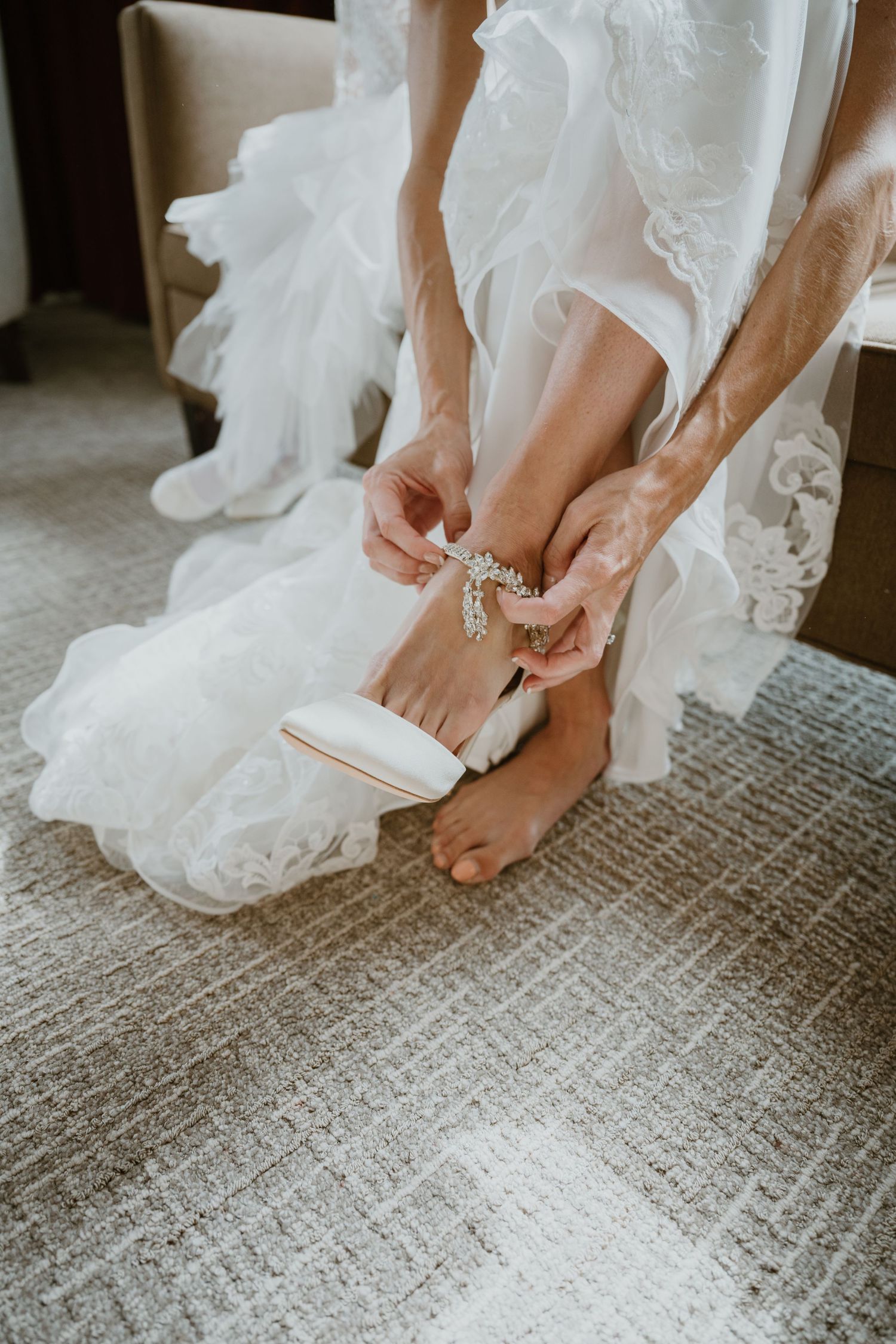Close-up of bride fastening a delicate crystal ankle strap on her elegant wedding shoe.
