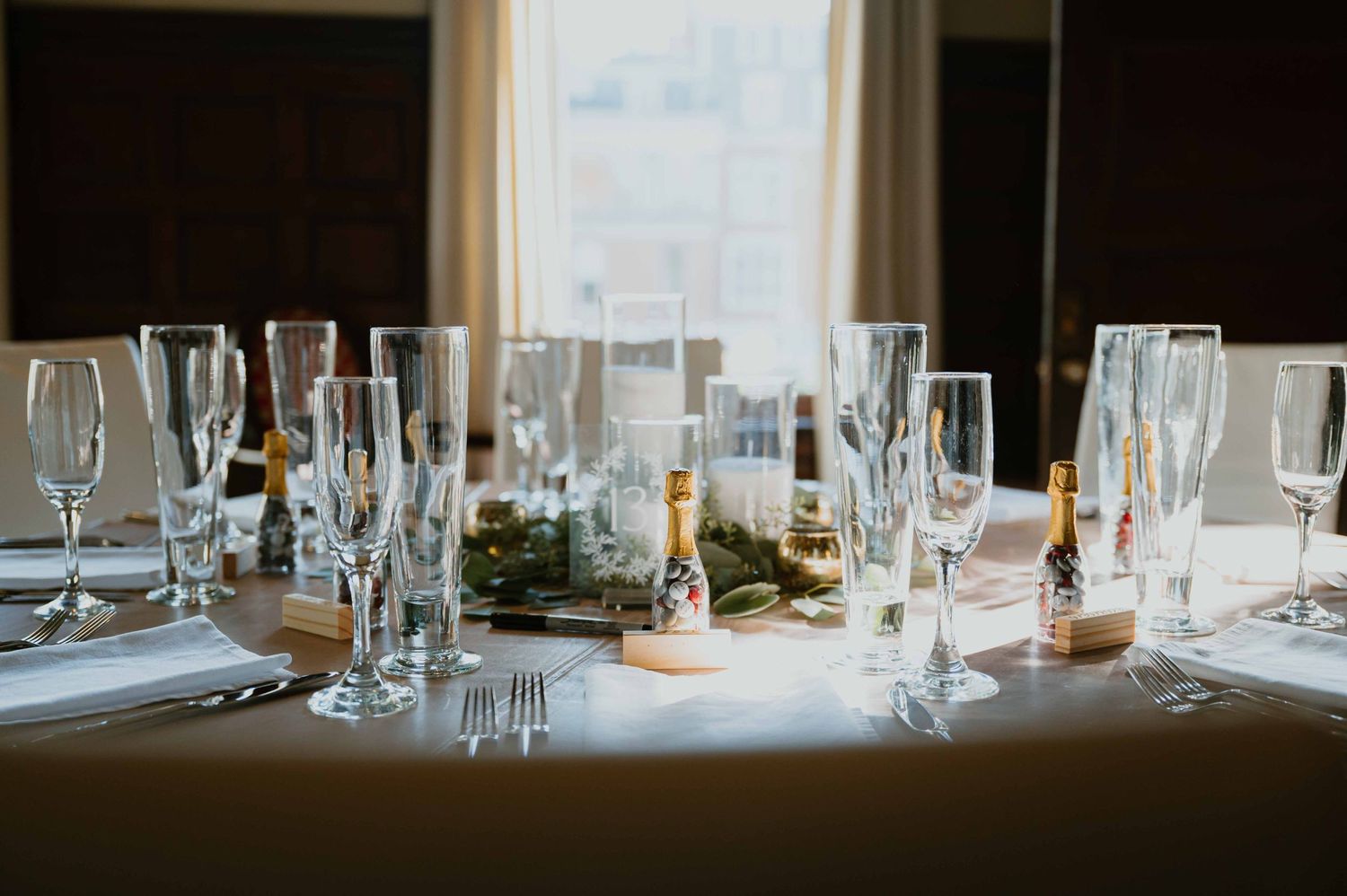Formal wedding reception table setting with crystal glassware, champagne bottles, and greenery centerpiece.