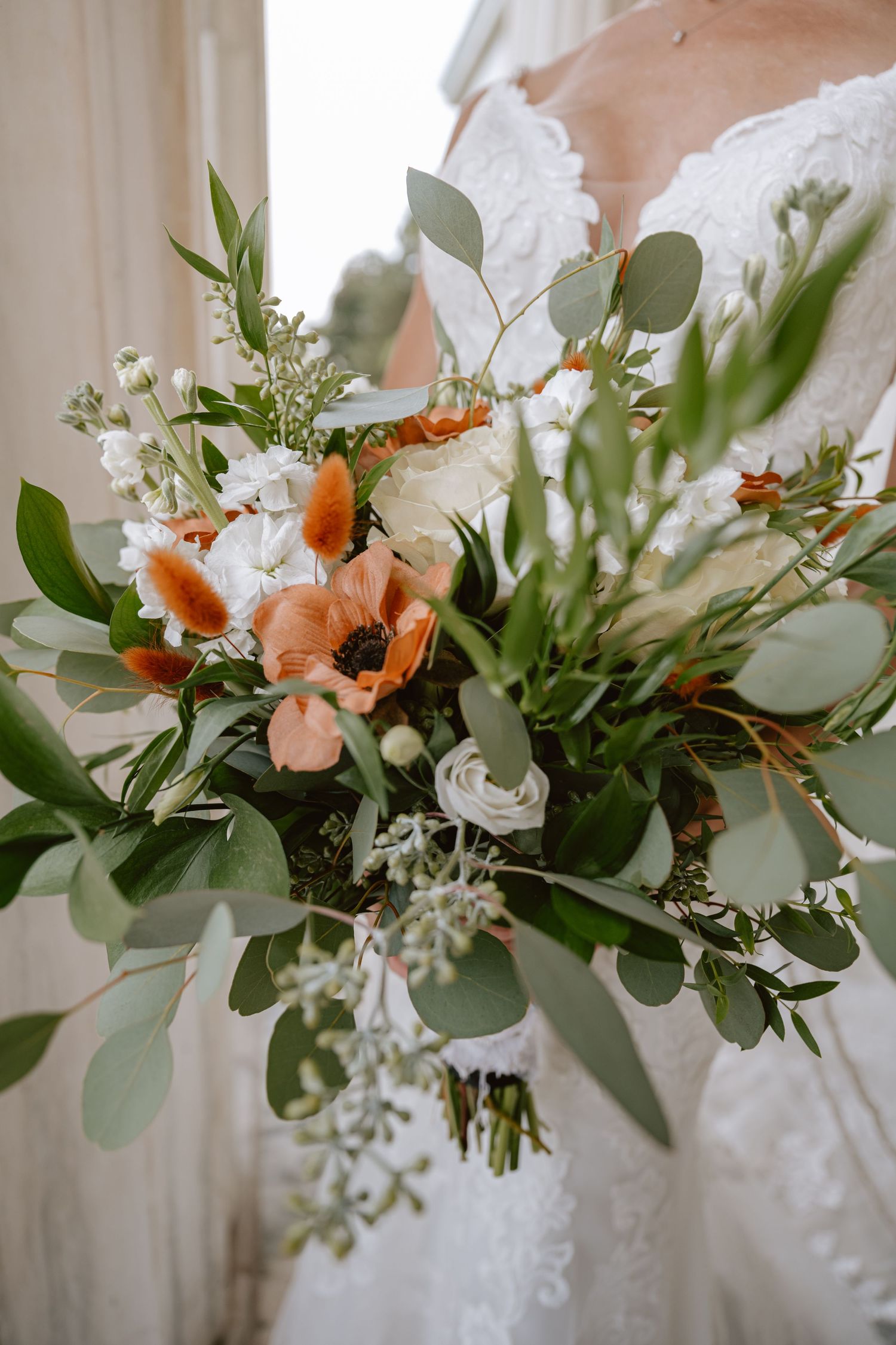 Bride holds a lush wedding bouquet featuring orange anemones, white roses, and eucalyptus greenery.