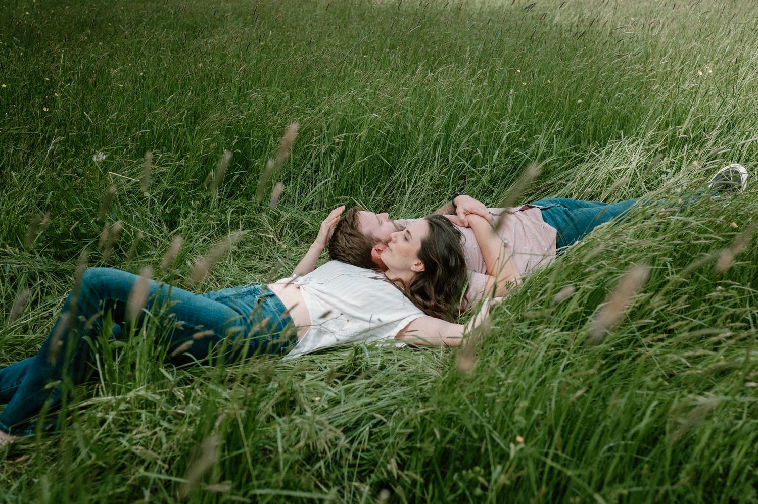 Couple lying in lush green grass facing each other in a romantic outdoor setting.