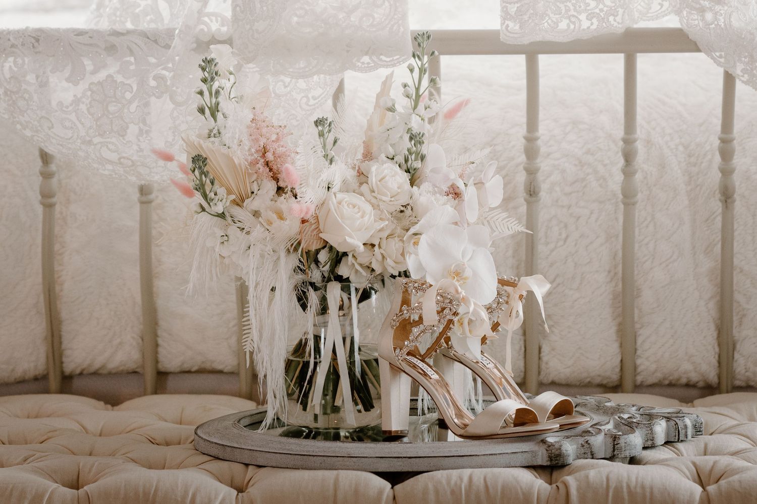 Elegant bridal flat lay featuring blush and white floral bouquet, strappy heels, and wedding rings.