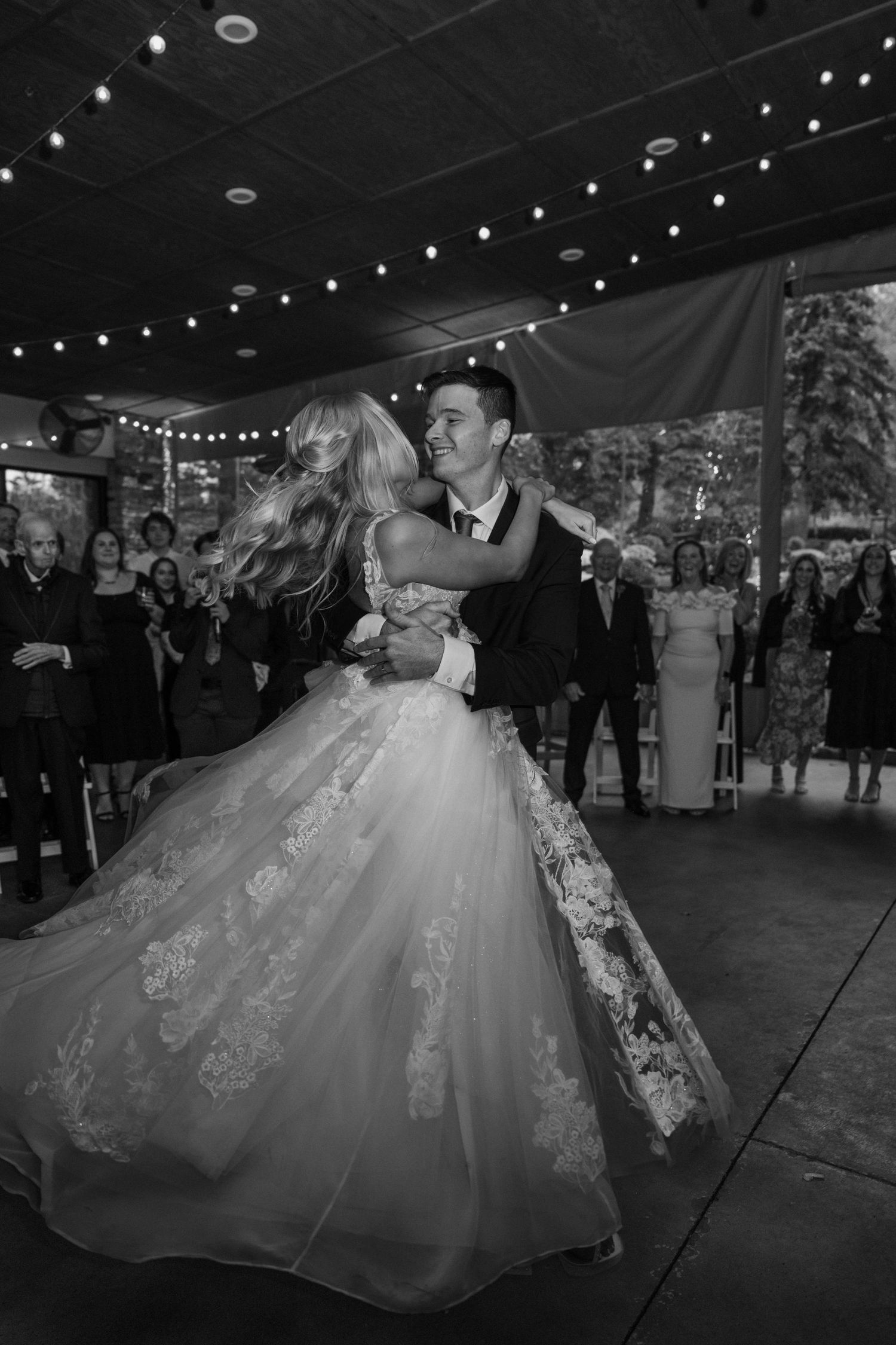Black and white photo of groom lifting bride during romantic first dance at wedding reception.
