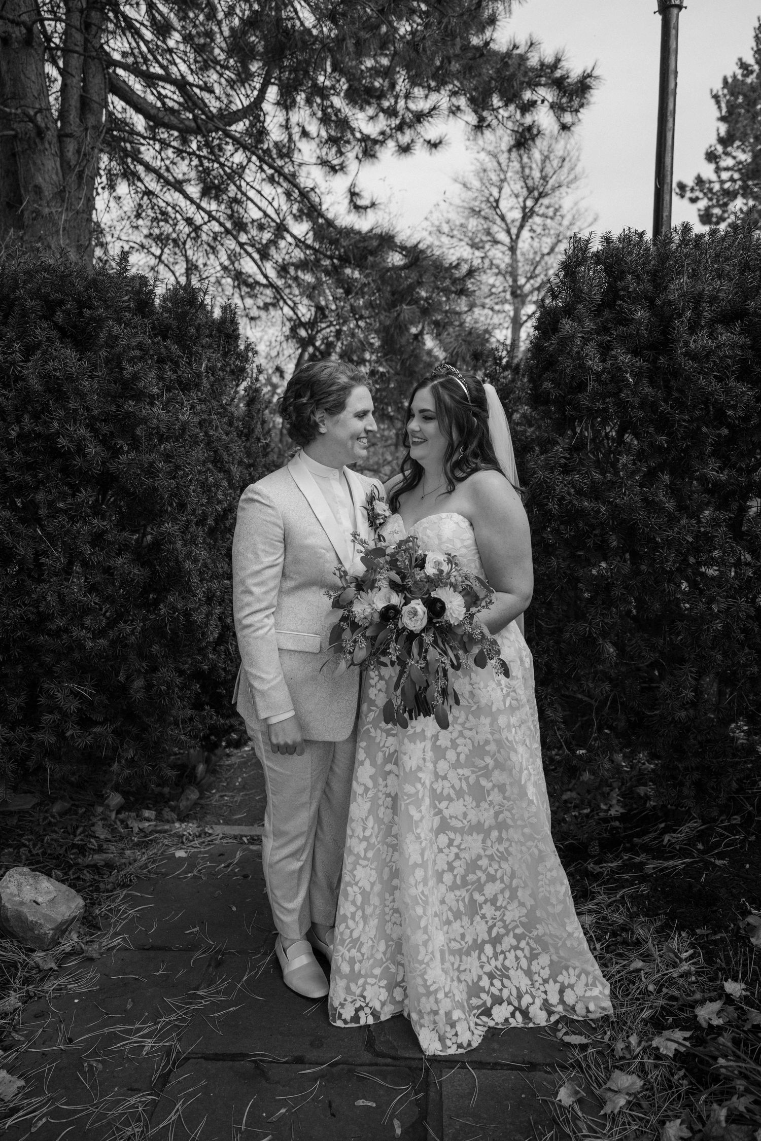 Black and white photo of wedding couple sharing a loving gaze in a garden setting with lush greenery.