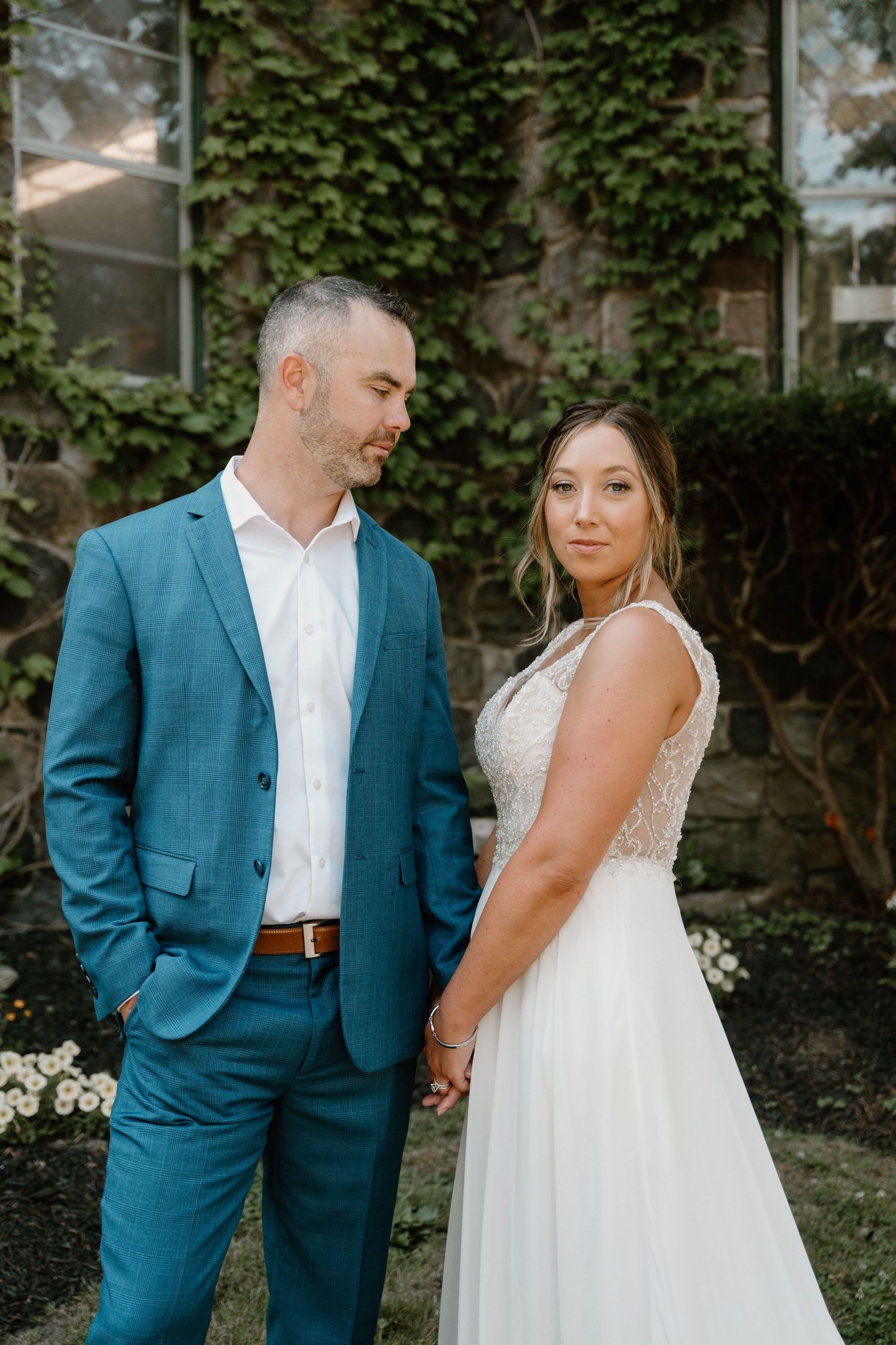 Bride and groom hold hands in front of ivy-covered stone building on wedding day.