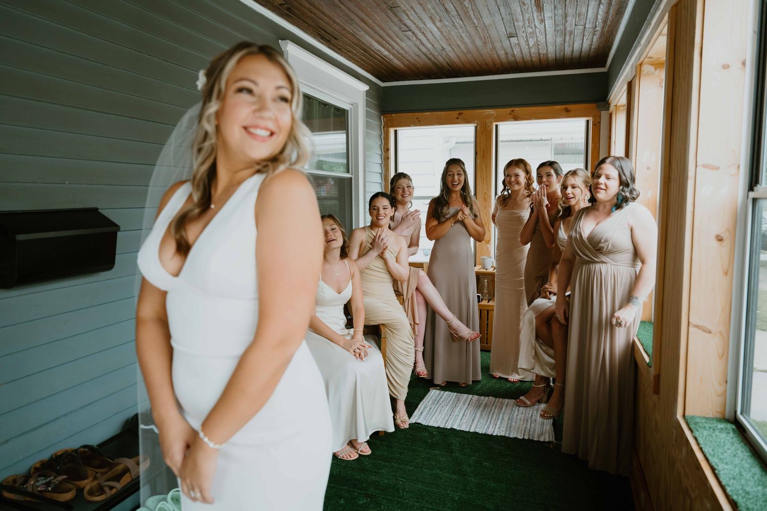 Excited bridesmaids in blush gowns react to bride's first look reveal on a porch.