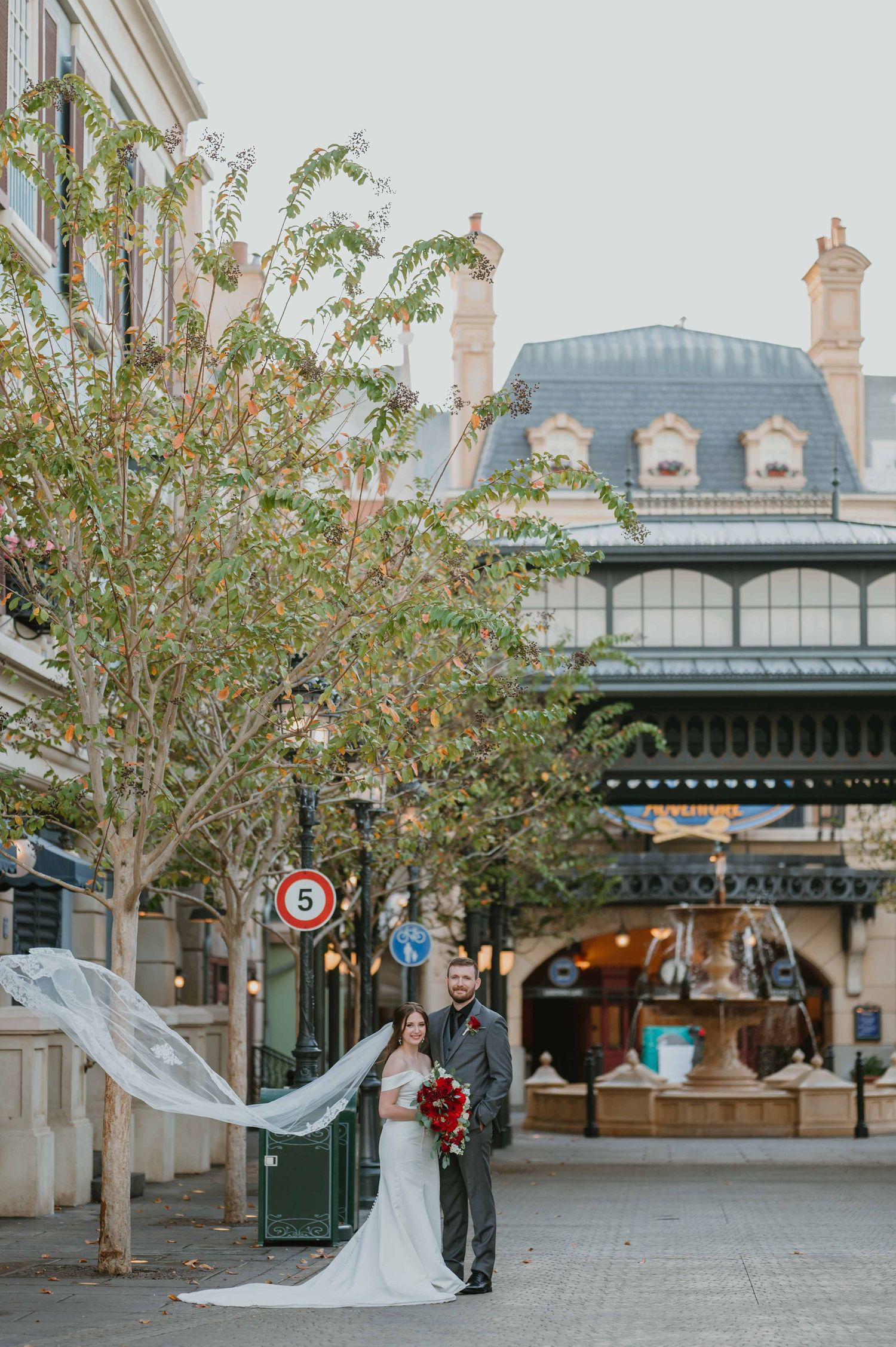 Bride and groom portrait with flowing veil in French-inspired plaza with European architecture.