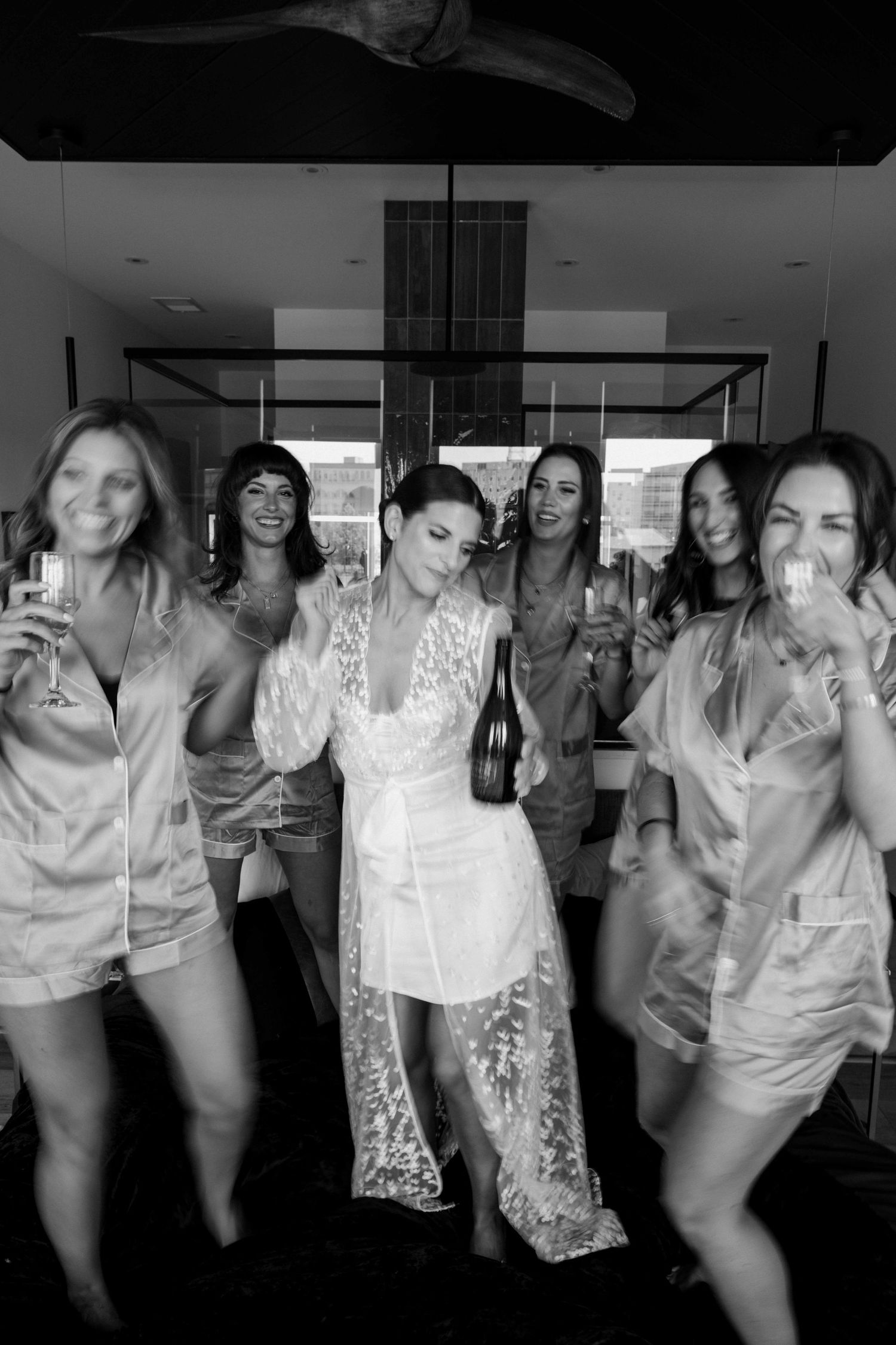 Black and white photo of bride holding champagne bottle celebrating with bridesmaids.