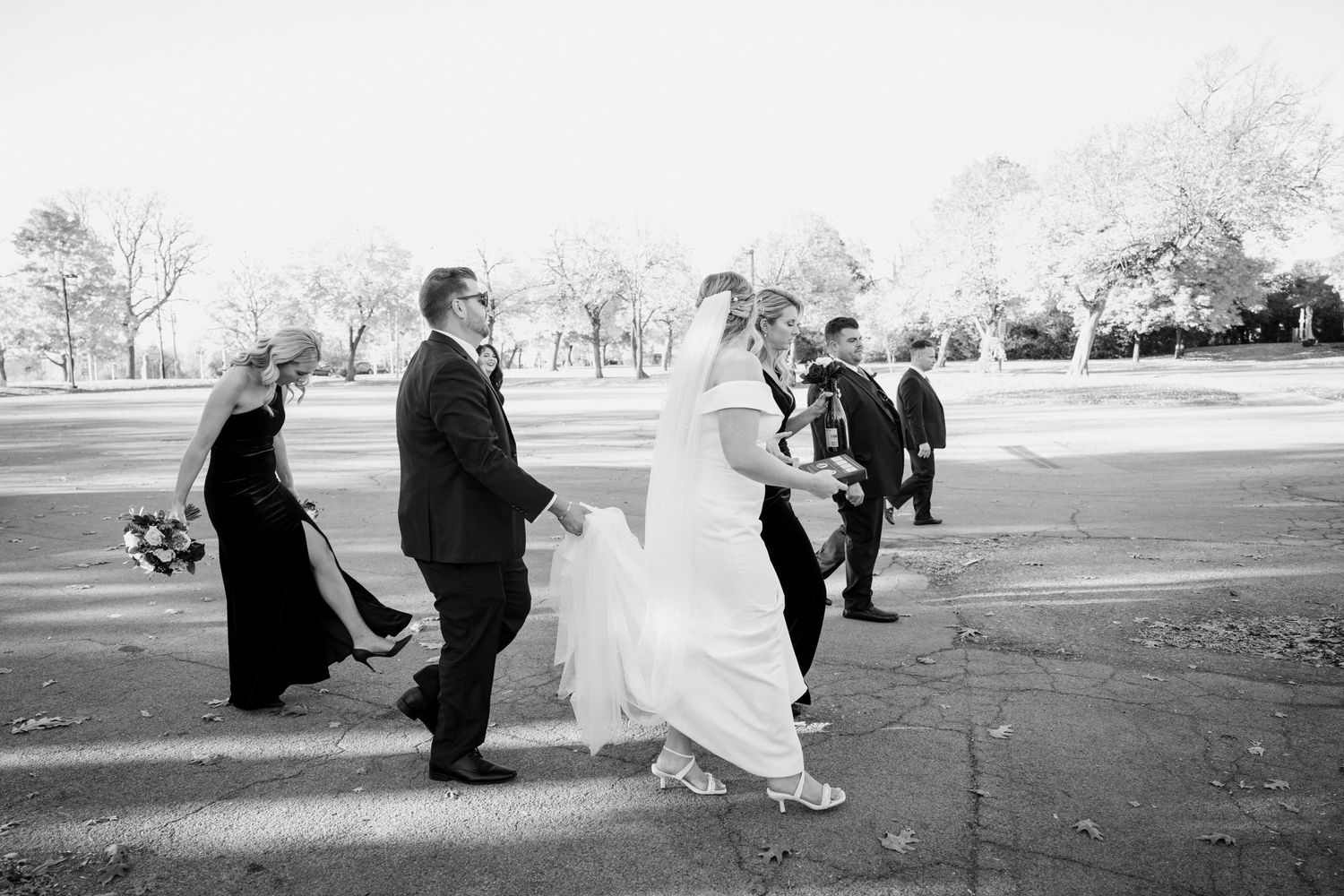 Black and white photo of bride, groom and wedding party crossing street together on wedding day.