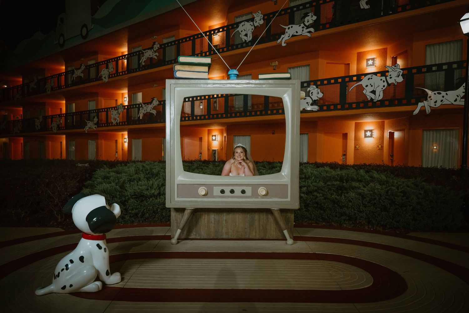 Woman posing inside giant vintage TV prop at Disney All-Star Movies Resort at night.