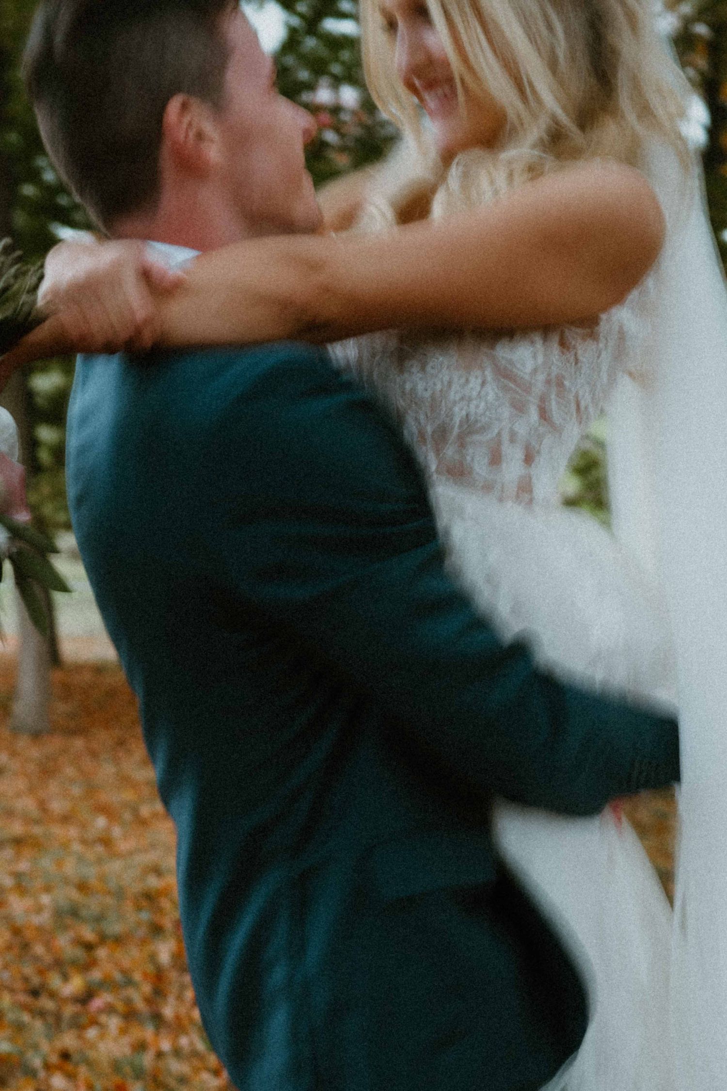 Groom lifting smiling bride in white lace gown among fall foliage.