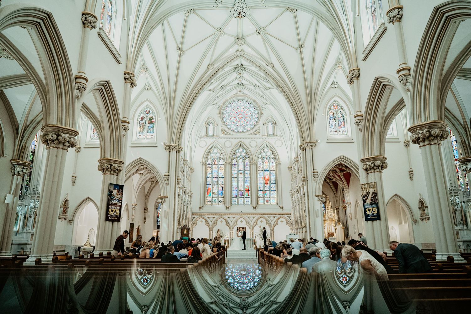 Stunning Gothic cathedral wedding ceremony with vaulted white arches and colorful stained glass windows.