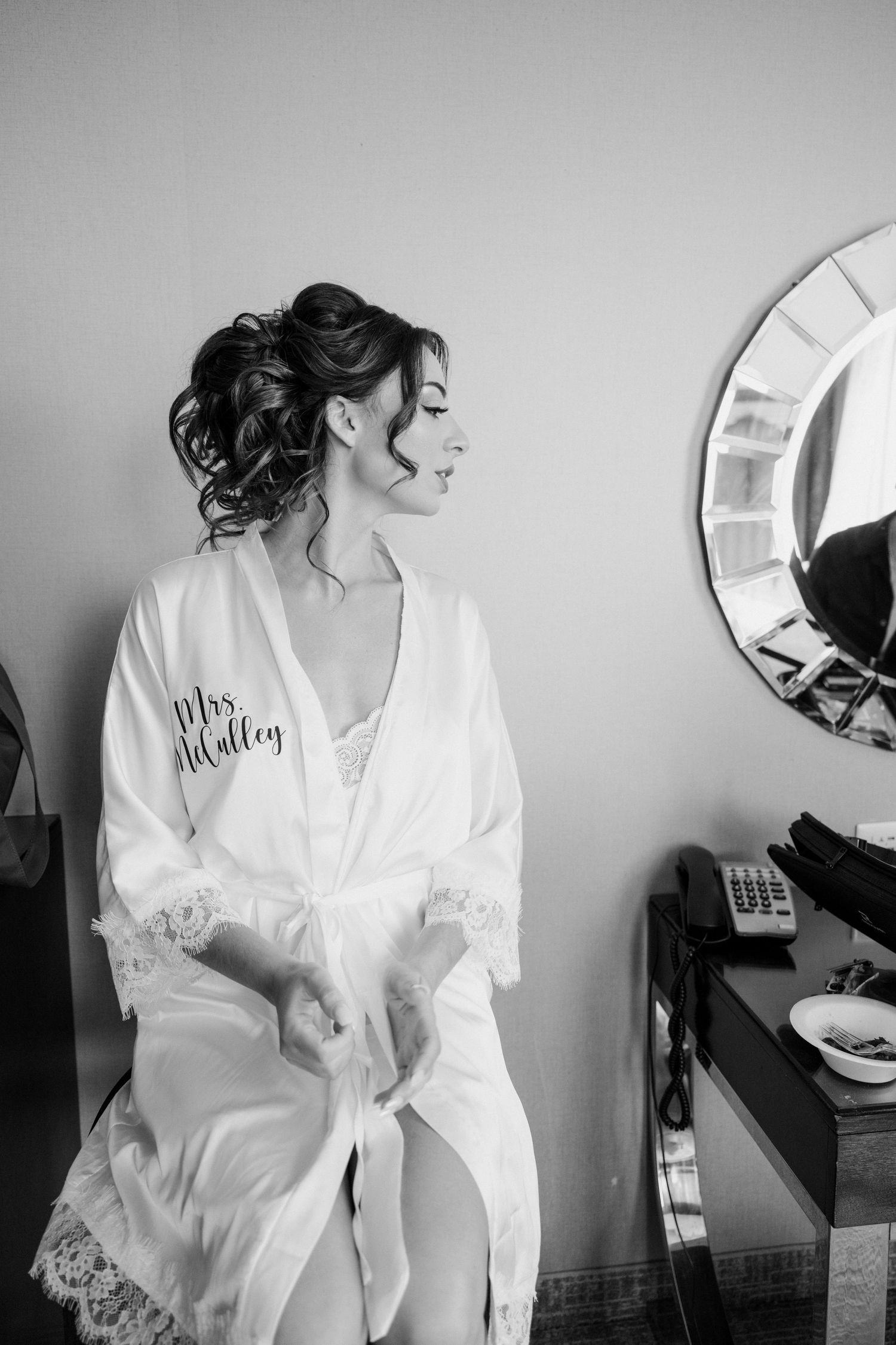 Bride in Mrs. robe smiling while getting ready on wedding day in black and white.