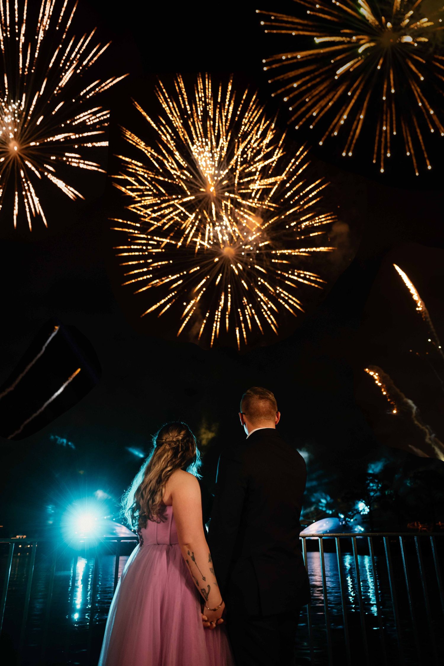 Couple holds hands watching stunning golden fireworks light up the night sky at wedding.
