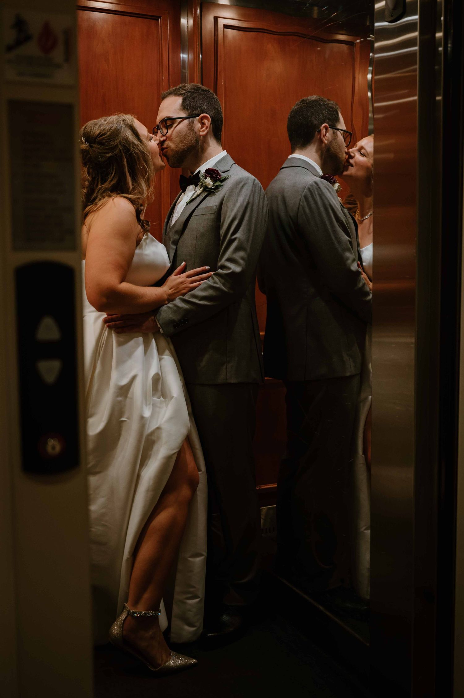 Bride and groom sharing a kiss reflected in elevator mirror in romantic portrait.